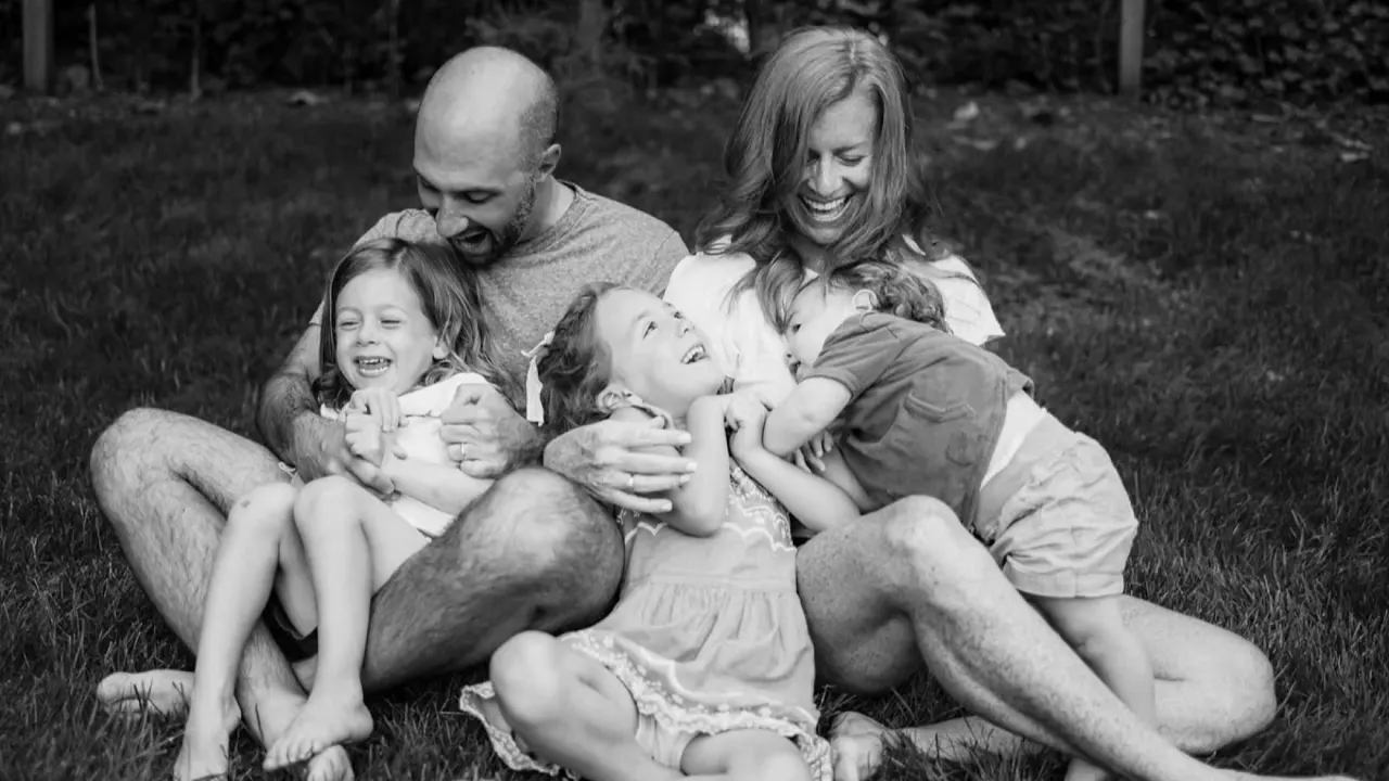 Kate, her husband and their three children laughing together on the grass, black and white photo